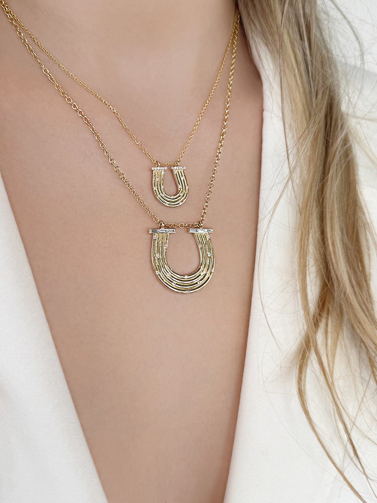 Lifestyle image featuring the 14K yellow gold Large Slim Reeded Baguette Diamond Horseshoe Necklace and the 14K yellow gold Slim Reeded Diamond Horseshoe Necklace by Sig Ward Jewelry, showcasing natural baguette and round diamond accents in elegant horseshoe-inspired fine jewelry designs.