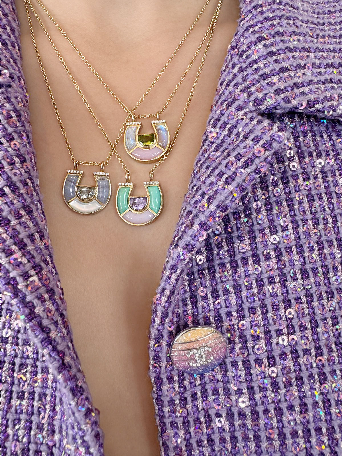 Model wearing layered 14K yellow gold horseshoe pendant necklaces with pastel gemstones, mother-of-pearl, and diamond accents by Sig Ward Jewelry.
