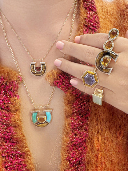 Lifestyle image featuring the 14K yellow gold Garnet, Tiger's Eye, and Diamond Horseshoe Necklace, Medium Citrine, Tiger's Eye, and Diamond Horseshoe Ring, and Jumbo Citrine, Chrysoprase, Tiger's Eye, Turquoise, and Baguette Diamond Horseshoe Necklace by Sig Ward Jewelry, showcasing natural garnet, citrine, chrysoprase, tiger's eye, turquoise, and diamond accents in elegant horseshoe-inspired fine jewelry designs.