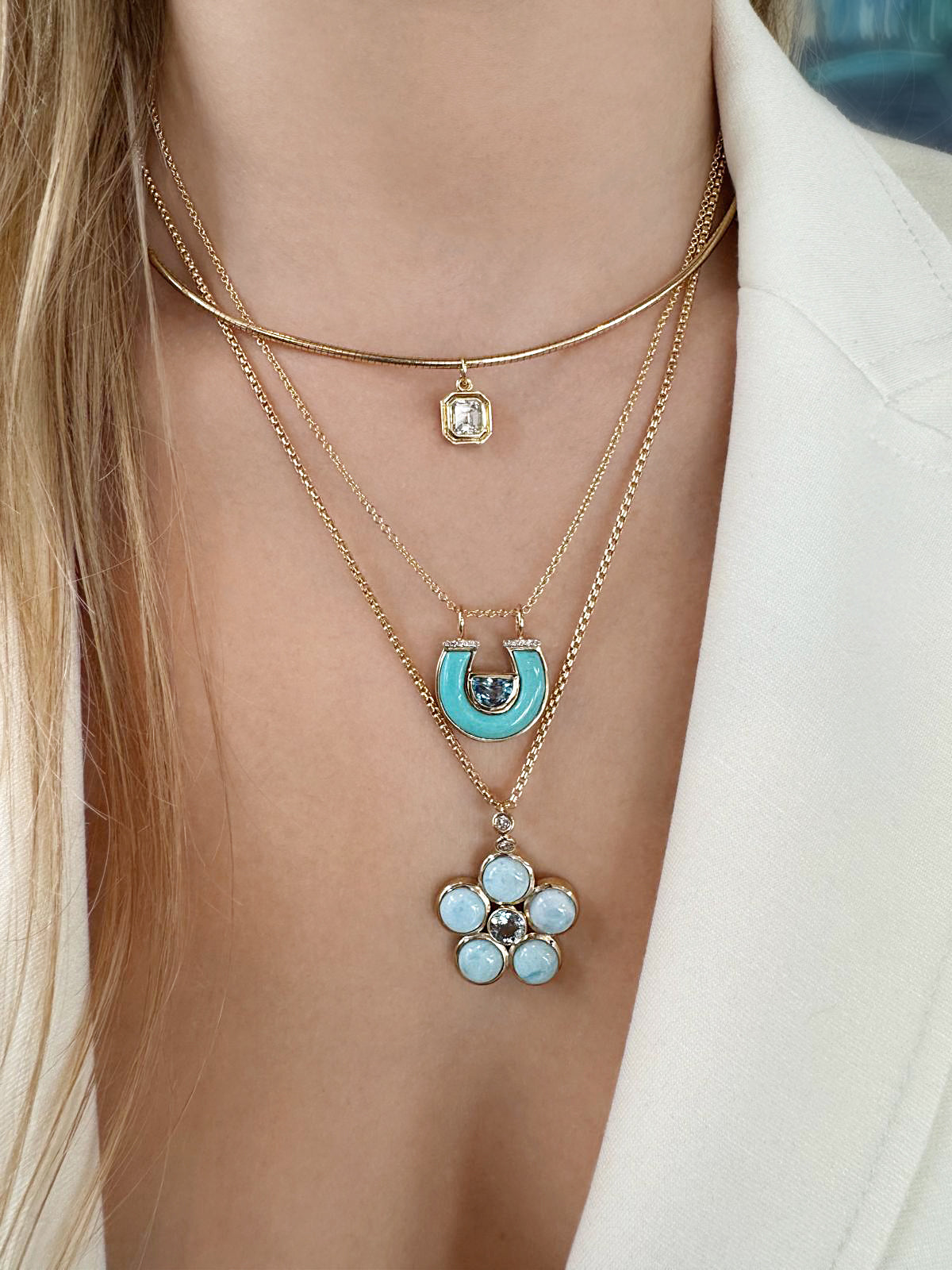 Lifestyle image featuring the 14K yellow gold Omega Asscher Cut Diamond Solitaire Collar, 14K yellow gold Larimar, Aquamarine, and Diamond Blossom Necklace, and 14K yellow gold Blue Topaz, Turquoise, and Diamond Horseshoe Necklace by Sig Ward Jewelry, showcasing an Asscher-cut diamond, natural larimar, aquamarine, blue topaz, turquoise, and diamond accents in elegant contemporary fine jewelry designs.