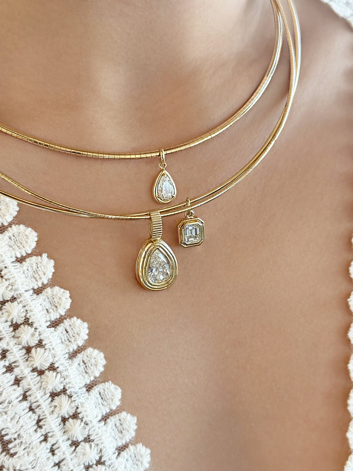 Lifestyle image featuring the 14K yellow gold Omega Pear Shape Diamond Solitaire Collar and 14K yellow gold Omega Asscher Cut Diamond Solitaire Collar by Sig Ward Jewelry, showcasing natural pear-shaped and Asscher-cut diamonds in elegant contemporary collar necklace designs.