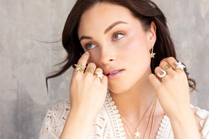 A model wearing a curated stack of Sig Ward Jewelry 14K gold and diamond pieces, including Star Power gemstone rings, layered star necklaces, and Manifest collection horseshoe statement rings.